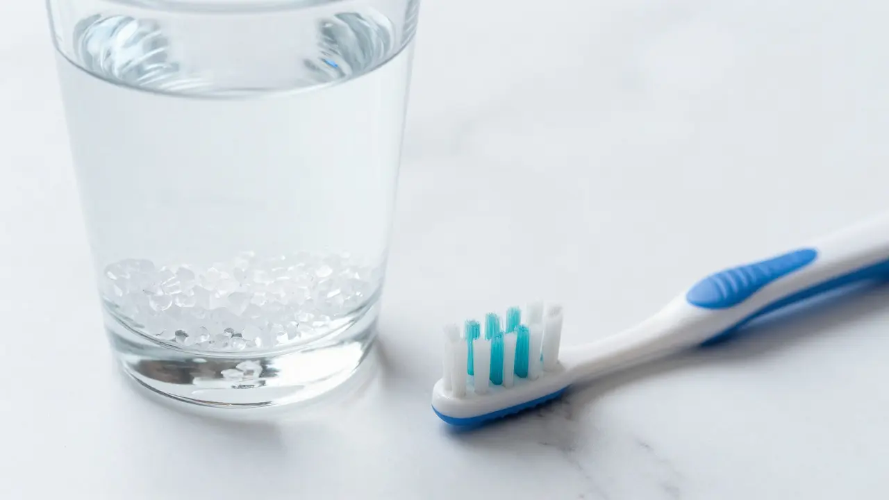 Kádran s vlažnou slanou vodou a mezizubním kartáčkem na bílém podkladu